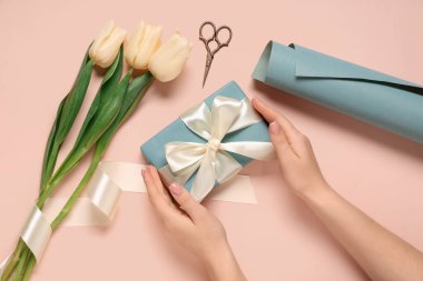 Hediye kutusu, laleler ve bej arka planda ambalaj kağıdı olan kadın elleri. Uluslararası Kadınlar Günü
