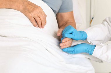 Hastane odasında el ele tutuşan, kıdemli hastası olan kadın doktor, yakın plan.