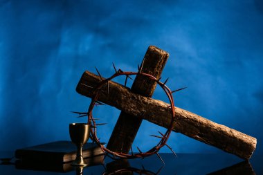 Dikenli taç haç, İncil ve şarap kadehi siyah masada mavi arka planda.