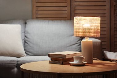 Geceleri oturma odasındaki masada kitap ve kahveyle parlayan lamba.