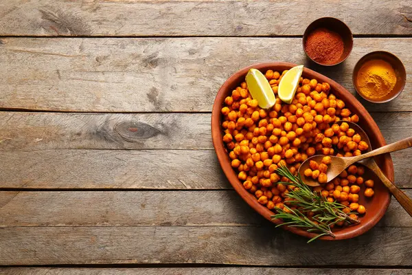 Ahşap arka planda biberiye, limon ve baharatlı bir kase lezzetli nohut.