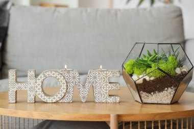 Oturma odasındaki masada yanan mumlar ve floraryum olan şık bir dekor.