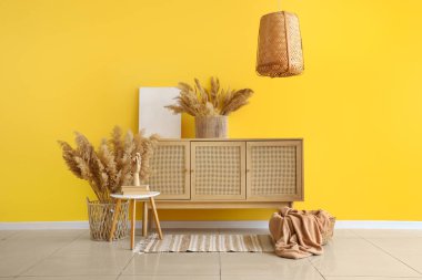Çekmeceler, kahve masası ve sarı duvarın yanındaki otlar.