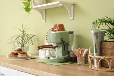 Modern kahve makinesi, fincanlar, karıştırıcılar ve çörekler mutfaktaki masada.