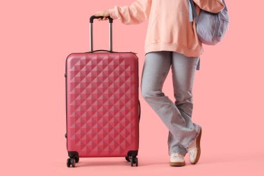 Pembe arka planda sırt çantası ve bavulu olan bir kadın turist.