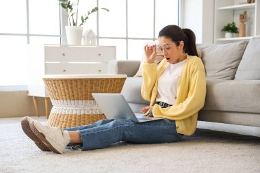 Evde dizüstü bilgisayar kullanan gözlüklü genç bir kadın şok oldu.