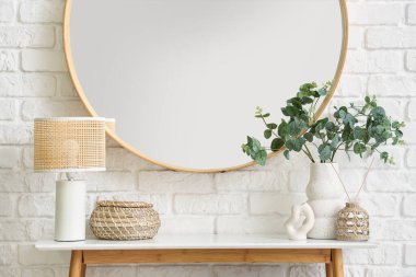 Dekorlu masa, beyaz tuğlalı duvardaki ev bitkisi ve ayna. Yakın çekim.