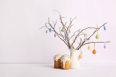 Renkli yumurtaları ve beyaz arka planda Paskalya pastaları olan bir sürahi ağaç dalı.