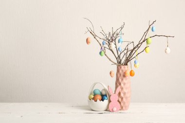 Ağaç dallı vazo ve beyaz ahşap masaya boyanmış Paskalya yumurtaları.