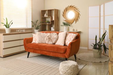 Modern oturma odasının içinde kahverengi kanepe, raf ünitesi ve şık bir ayna var.