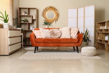 Modern oturma odasının içinde kahverengi kanepe, raf ünitesi ve şık bir ayna var.