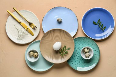 Paskalya yumurtalı farklı temiz tabaklar, taze yeşil yapraklar ve bej arka planda çingene çiçekleri.