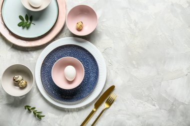 Paskalya yumurtaları ve gri arka planda taze yeşil yapraklarla farklı temiz tabaklar.