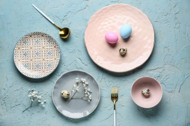 Farklı temiz tabaklar, paskalya yumurtaları ve mavi arka planda güzel çigila çiçekleri.
