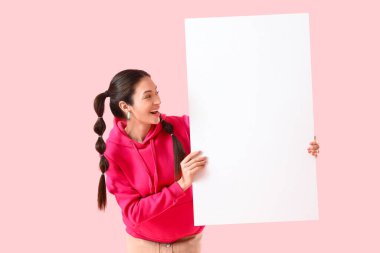 Pembe arka planda boş posteri olan kapüşonlu şık genç bir kadın.