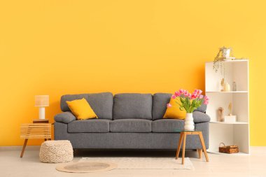 Gri kanepesi, raf ünitesi ve kahve masasında güzel lale çiçekleri olan şık bir oturma odası.