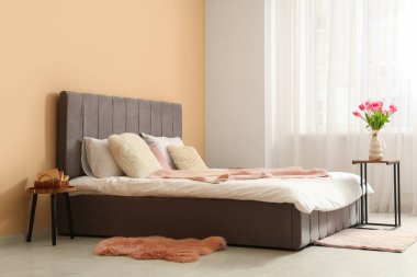 Şık oturma odasının içinde rahat bir yatak ve komodinin üzerinde güzel lale çiçekleri var.