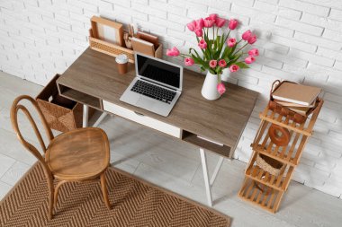 Modern dizüstü bilgisayarlı şık çalışma alanı, bir fincan kahve ve beyaz tuğla duvarın yanında güzel lale çiçekleri.