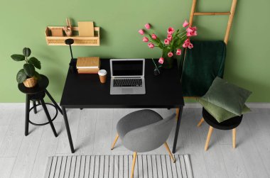 Modern dizüstü bilgisayarı, kitapları ve yeşil duvarın yanındaki güzel lale çiçekleriyle süslü çalışma alanı.