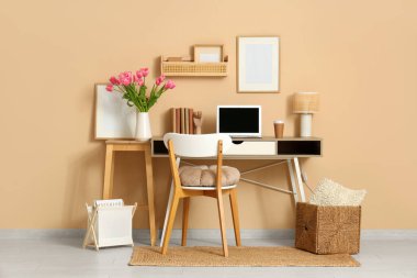 Modern dizüstü bilgisayar, kitaplar ve bej duvarın yanında güzel lale çiçekleri olan şık bir çalışma alanı.