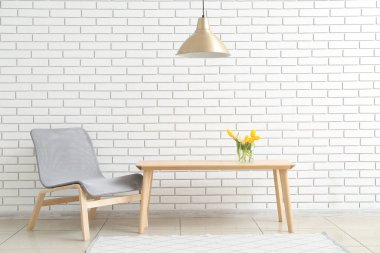 Modern grey armchair and table near white brick wall