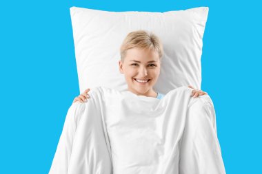 Mavi arka planda yumuşak battaniye ve yastıklı genç bir kadın.