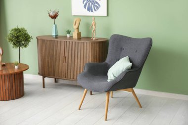 Yastığı, şifoniyeri ve yeşil duvarın yanındaki sehpası olan koyu gri koltuk.