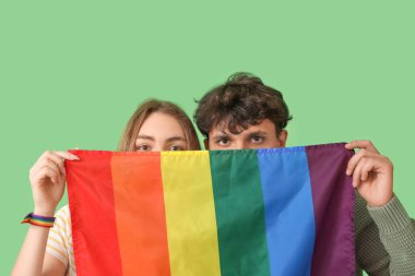 Yeşil arka planda LGBT bayrağı olan genç çift, yakın plan.