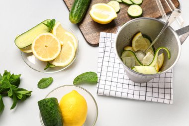 Beyaz zemin üzerinde salatalık limonatası hazırlamak için malzemelerle dolu kova ve kaseler.