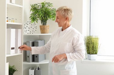 Kadın doktor klinikteki raftan klasör alıyor.