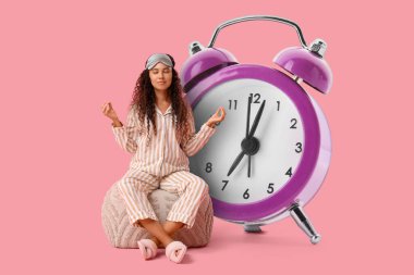 Pijamalı güzel bir Afro-Amerikalı kadın pembe arka planda puf üzerinde meditasyon yapıyor.