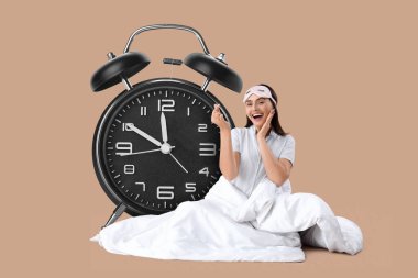 Büyük çalar saat ve bej arka planda battaniyesi olan mutlu genç kadın.