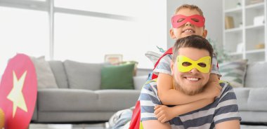 Süper kahraman kostümü giymiş babasıyla evde yerde yatan küçük bir çocuk.