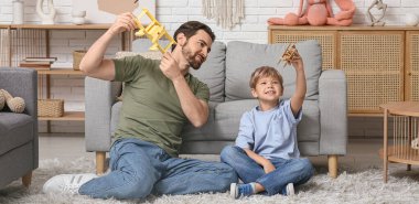 Baba ve küçük oğlu oturma odasında yerde tahta uçaklarla oynuyorlar. Babalar Günü.