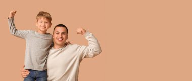 Mutlu baba ve küçük oğlu bej arka planda kaslarını gösteriyor.