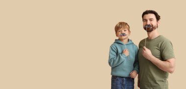 Baba ve küçük oğlu bej arka planda kağıt bıyık tutuyorlar ve mesaj için yer var. Babalar Günü.