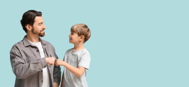 Baba ve küçük oğlu açık mavi arka planda yumruk tokuşturup mesaj atıyorlar. Babalar Günü.