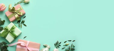 Dekoratif tavşancık, hediye kutuları, çiçekler ve turkuaz arka planda yeşil yapraklar yazı için yer var. Paskalya kutlaması