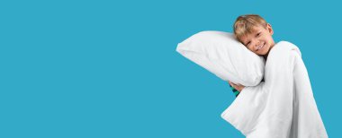 Pijamalı, yastıklı ve battaniyeli açık mavi arka planda mesaj için yeri olan mutlu bir çocuk.