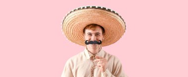 Fötr şapkalı ve pembe arka planda kağıt bıyıklı komik bir genç.