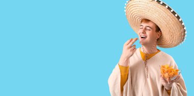 Açık mavi arka planda nachos yiyen genç Meksikalı adamın portresi.