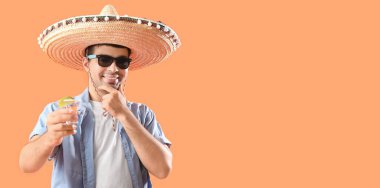 Sombrero 'lu genç adam turuncu arka planda tekila içiyor ve mesaj için yeri var.