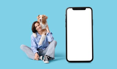 Güzel bir genç bayan mavi arka planda şirin bir Avustralya çoban köpeğiyle oturuyor.