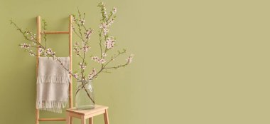 Yeşil duvarın yanındaki merdivende çiçek açan ağaç dalları olan vazo. Tasarım için pankart