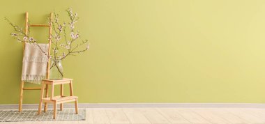 Yeşil duvarın yanındaki merdivende çiçek açan ağaç dalları olan vazo. Tasarım için pankart