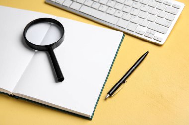 Blank open book, magnifier, pen and keyboard on yellow background, closeup. World Poetry Day celebration