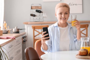 Mutfakta cep telefonu ve bir bardak meyve suyu olan genç bir kadın.