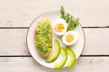 Hafif ahşap arka planda avokadolu lezzetli bir bruschetta tabağı.