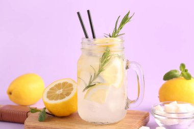 Ahşap pano ve eflatun arkaplanda taze limonata bulunan mason kavanozu.