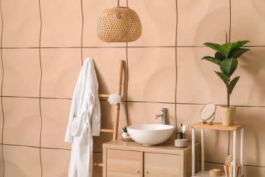 Bornozlu, lavabolu ve ahşap dolaplı banyo aksesuarları.